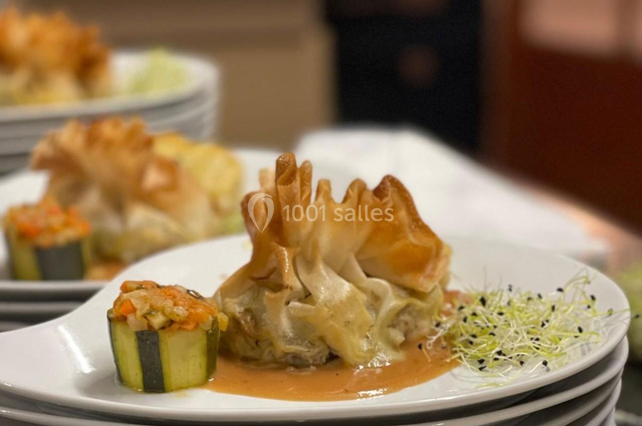 Assiette gastronomique avec une aumônière dorée, une courgette farcie et une sauce, accompagnées de jeunes pousses.