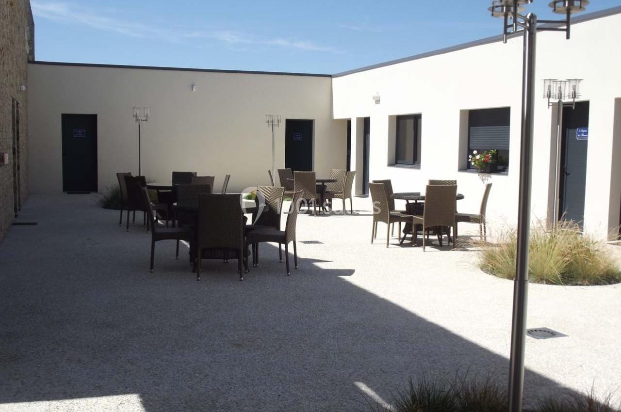 Cour intérieure avec mobilier de jardin en rotin, entourée de murs clairs et éclairée par un ciel dégagé.