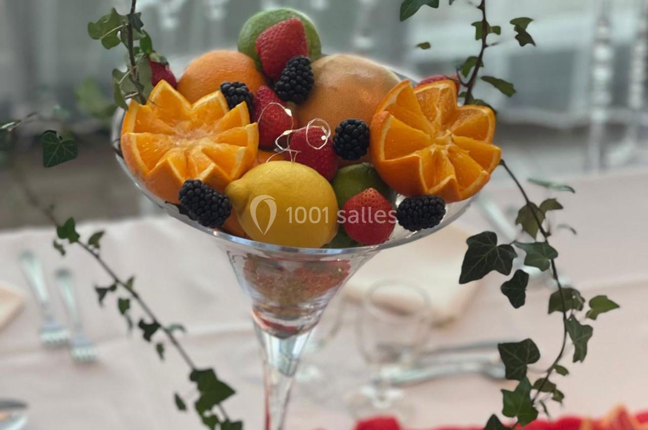 Coupe en verre garnie de fruits frais variés, dont oranges, citron, baies et feuilles de lierre décoratives.