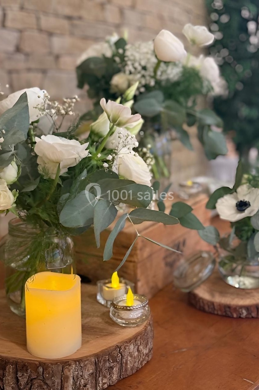 Bouquets de fleurs blanches et feuillages verts disposés sur des rondins de bois avec des bougies allumées.