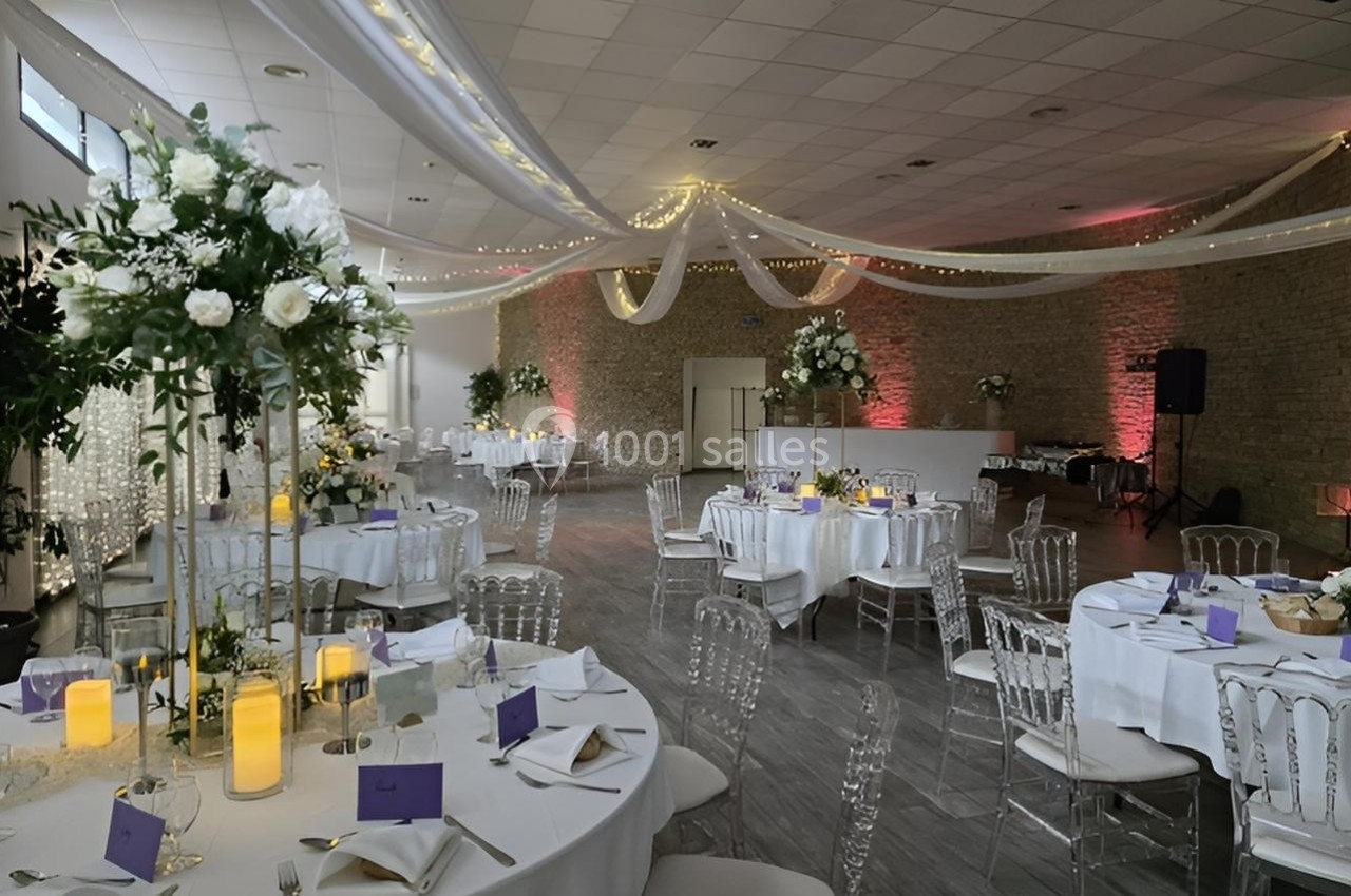 Salle de réception décorée avec des tables rondes, nappes blanches, chandelles et arrangements floraux élégants.