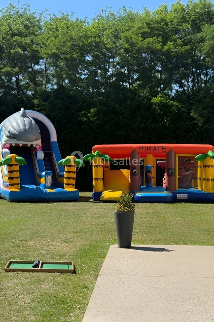 Deux structures gonflables colorées sur un thème marin et pirate installées sur une pelouse, entourées de verdure.