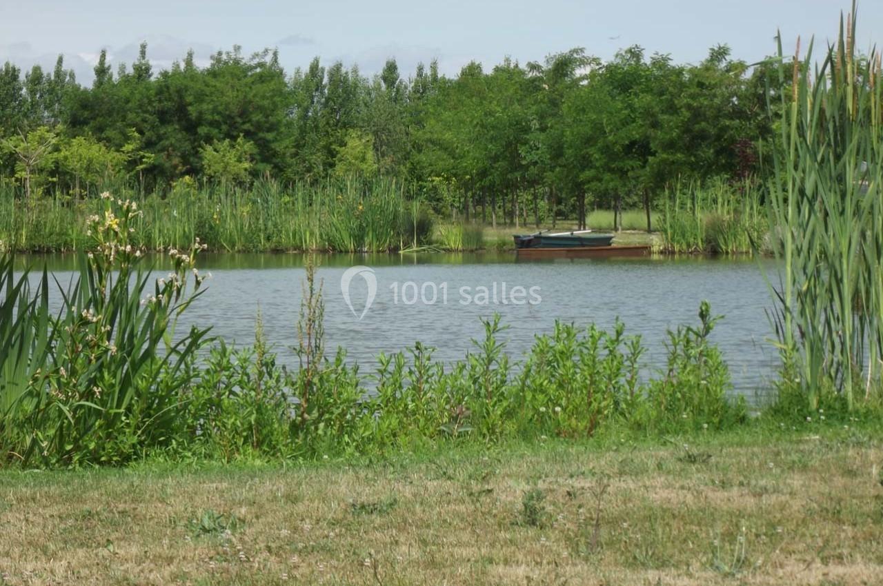 Vue d'un étang entouré de végétation avec un bateau amarré au loin et des arbres en arrière-plan.