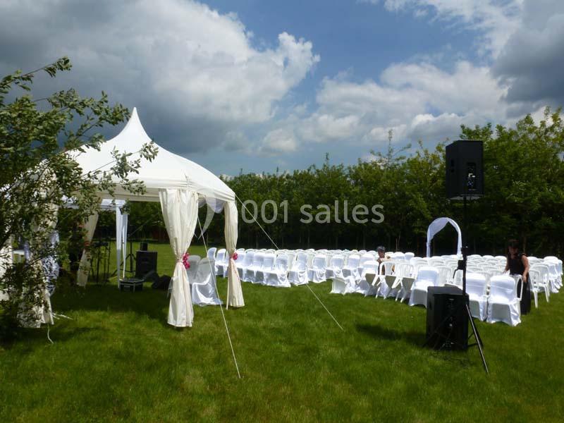 Chaises blanches disposées en rangées sur une pelouse, avec une tente blanche et des haut-parleurs en extérieur.