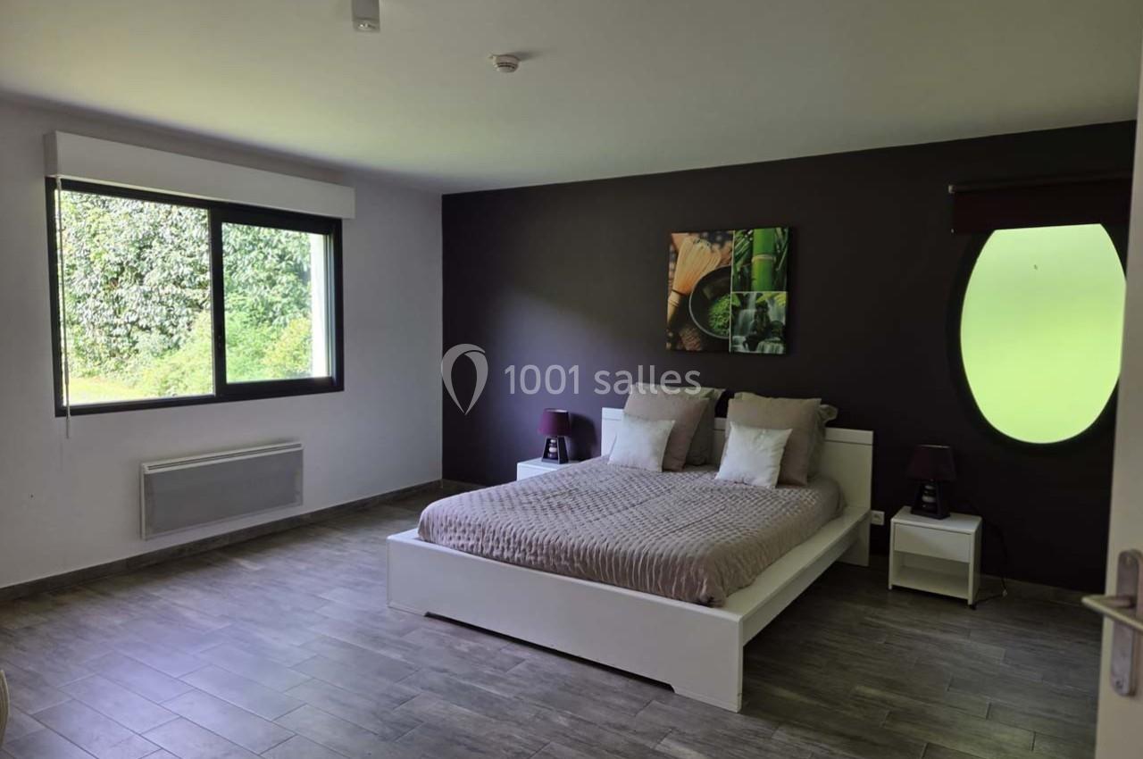 Chambre moderne avec lit double, mur violet, grande fenêtre donnant sur un jardin et sol en carrelage gris.