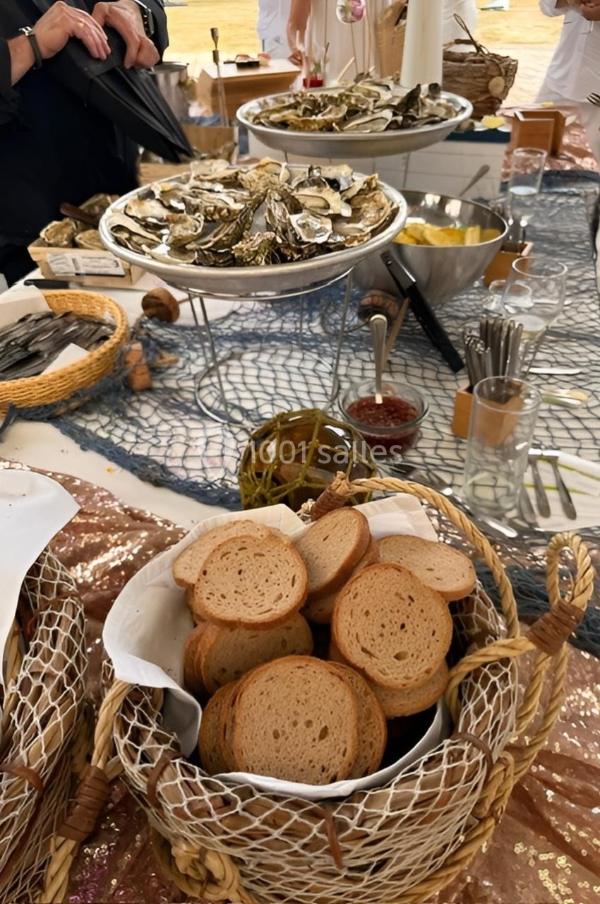 Plateau d'huîtres et paniers de pain grillé disposés sur une table décorée avec un filet de pêche.