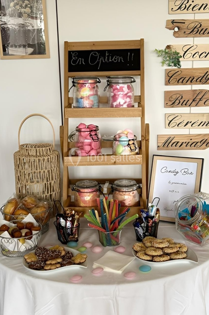 Table garnie de bonbons, biscuits et pâtisseries, avec des bocaux et un panneau ’En Option !!’ sur une étagère.