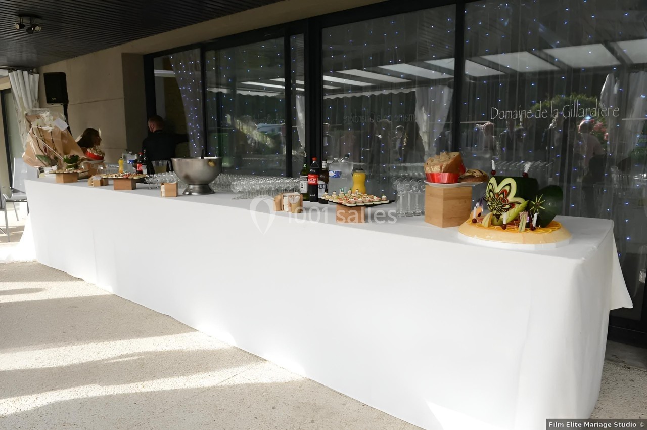 Table de buffet dressée avec nappes blanches, boissons, plats variés et décorations, devant une baie vitrée.