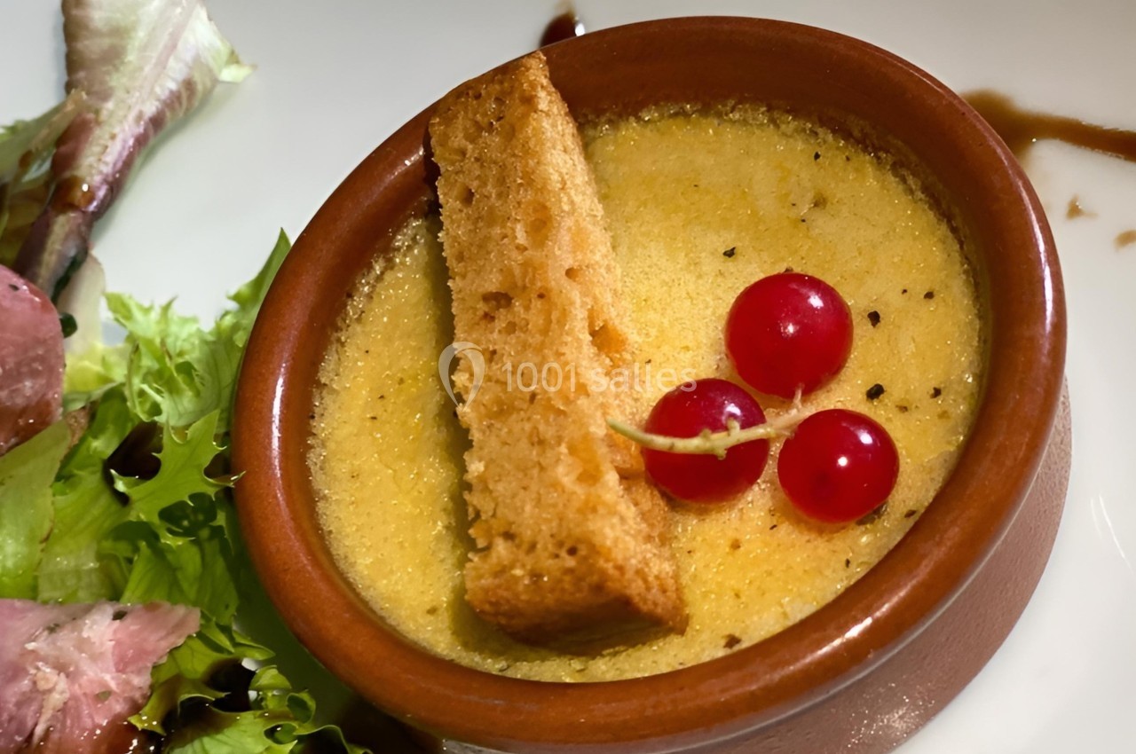 Crème brûlée salée servie avec un croûton, groseilles rouges et salade verte en accompagnement.
