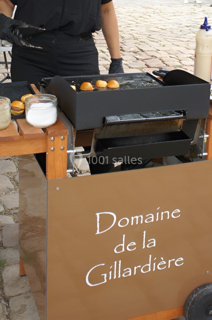 Personne préparant des mini-burgers sur une plancha mobile avec condiments et ingrédients à proximité.