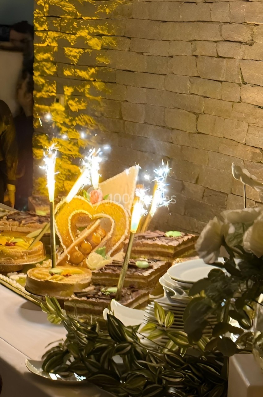 Table décorée avec des desserts, pièce montée en forme de cœur et fontaines lumineuses allumées, devant un mur en pierre.