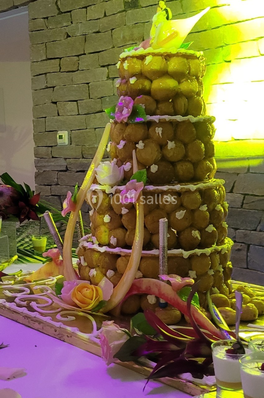 Pièce montée en choux décorée de fleurs et de sucre, présentée sur une table lors d'une réception.
