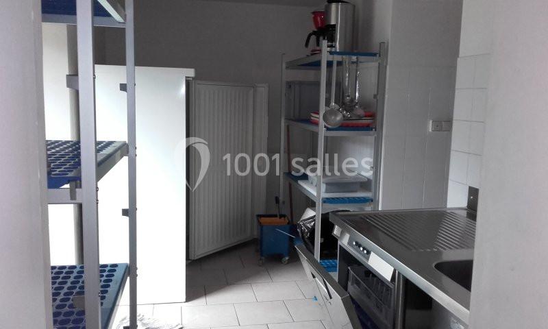 Cuisine professionnelle avec étagères métalliques, évier en inox, réfrigérateur et équipements de rangement.