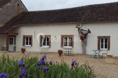 Bouteilles de jus de pomme, pot de confiture et noix disposés sur une nappe rouge à pois, avec un plat vert en arrière-plan.