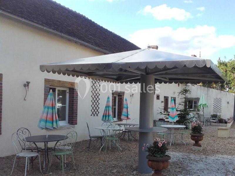Terrasse avec tables, chaises en métal et parasols colorés devant un bâtiment à façade claire.