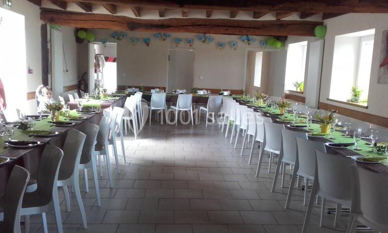 Salle décorée avec des tables alignées et dressées pour un événement, avec des guirlandes et des ballons suspendus.