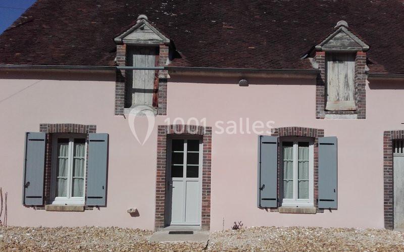 Façade d'une maison ancienne avec murs roses, volets bleus, fenêtres à petits carreaux et toit en tuiles sombres.