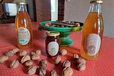 Bouteilles de jus de pomme, pot de confiture et noix disposés sur une nappe rouge à pois, avec un plat vert en arrière-plan.