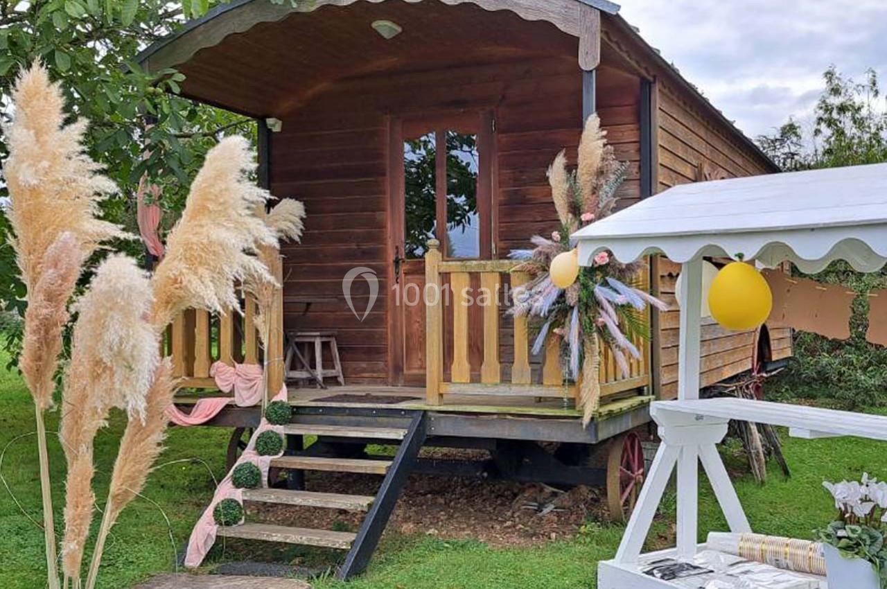 Roulotte en bois avec terrasse décorée de fleurs et de ballons, entourée de végétation et d'herbes de la pampa.