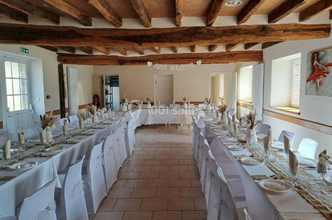 Salle de réception décorée pour un mariage, avec de longues tables dressées et une bannière ’Just Married’.