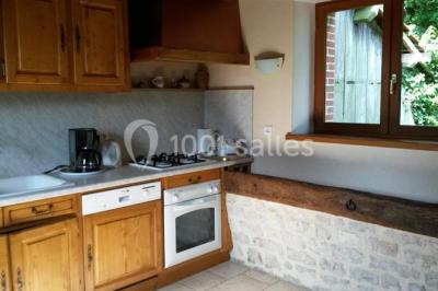 Bouteilles de jus de pomme, pot de confiture et noix disposés sur une nappe rouge à pois, avec un plat vert en arrière-plan.