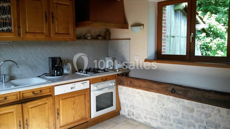 Cuisine rustique avec meubles en bois, évier, lave-vaisselle, four, plaques de cuisson et fenêtre donnant sur un jardin.