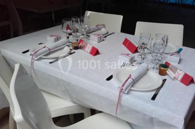 Bouteilles de jus de pomme, pot de confiture et noix disposés sur une nappe rouge à pois, avec un plat vert en arrière-plan.