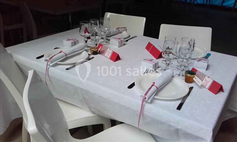 Table dressée avec nappe blanche, couverts, verres, serviettes roulées et décorations rouges et blanches.