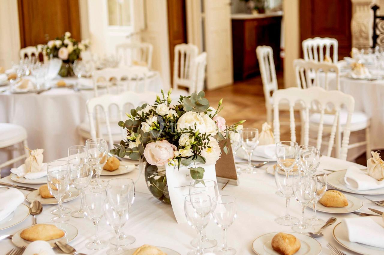 Salle de réception élégante avec tables dressées, nappes blanches, vaisselle raffinée et centre de table floral.