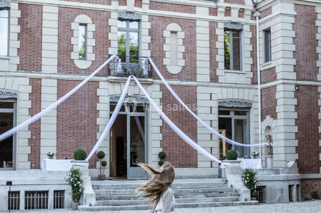 Une fillette en robe blanche court sur une pelouse devant une grande bâtisse en briques décorée pour un événement.