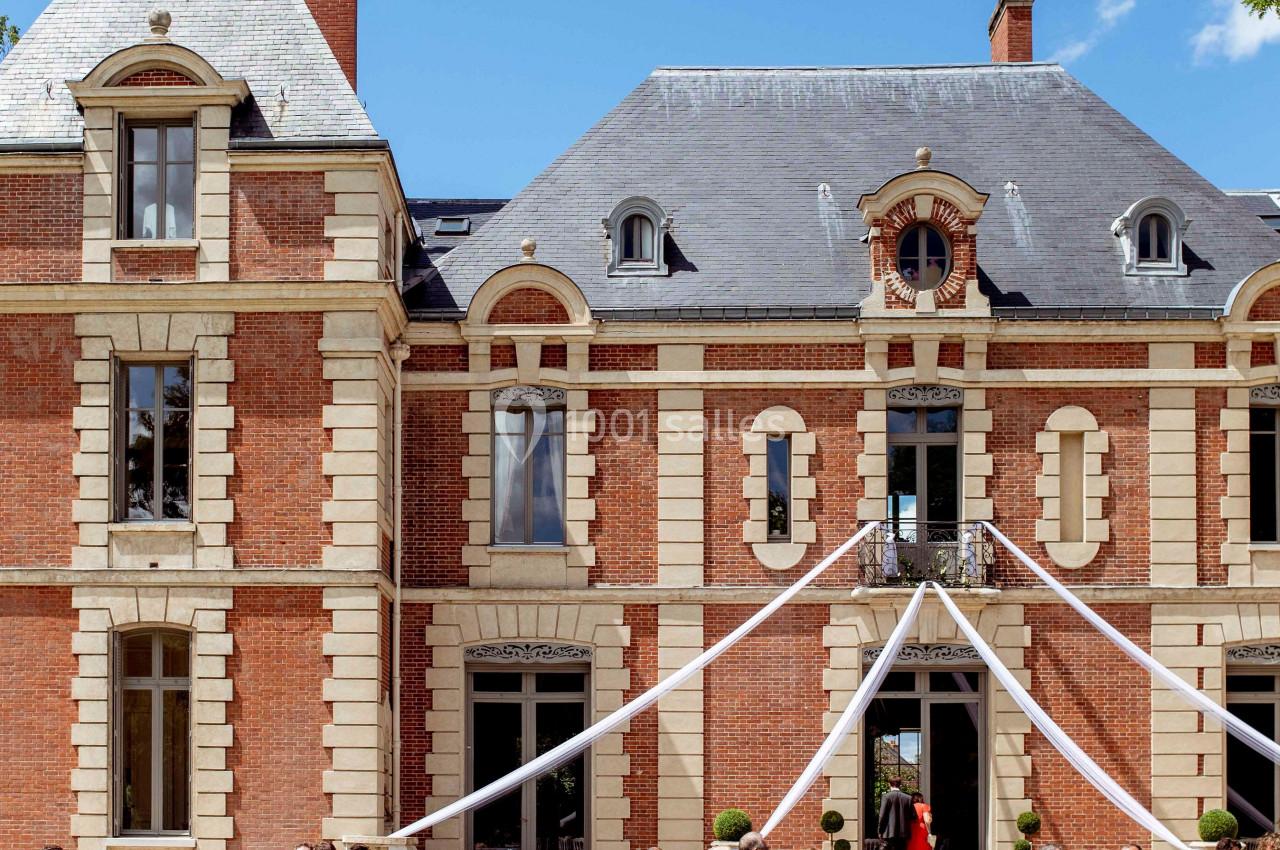 Groupe de personnes rassemblées devant un château en briques rouges lors d'un événement sous un ciel dégagé.