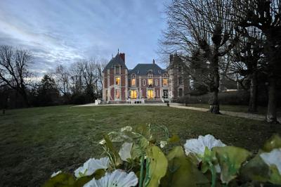 Façade d'un château éclairé au crépuscule, vue depuis un parterre de fleurs au premier plan.