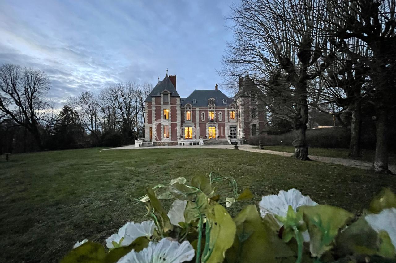 Façade d'un château éclairé au crépuscule, vue depuis un parterre de fleurs au premier plan.