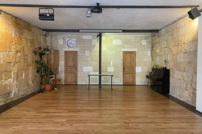 Salle vide avec parquet en bois clair, murs en pierre et en blanc, éclairage au plafond et grande baie vitrée au fond.