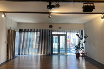 Salle vide avec parquet en bois clair, murs en pierre et en blanc, éclairage au plafond et grande baie vitrée au fond.