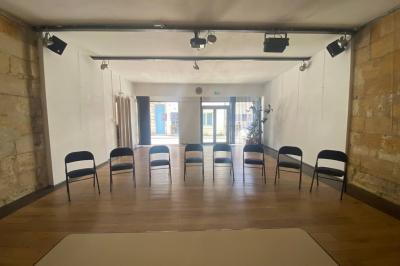 Salle vide avec parquet en bois clair, murs en pierre et en blanc, éclairage au plafond et grande baie vitrée au fond.