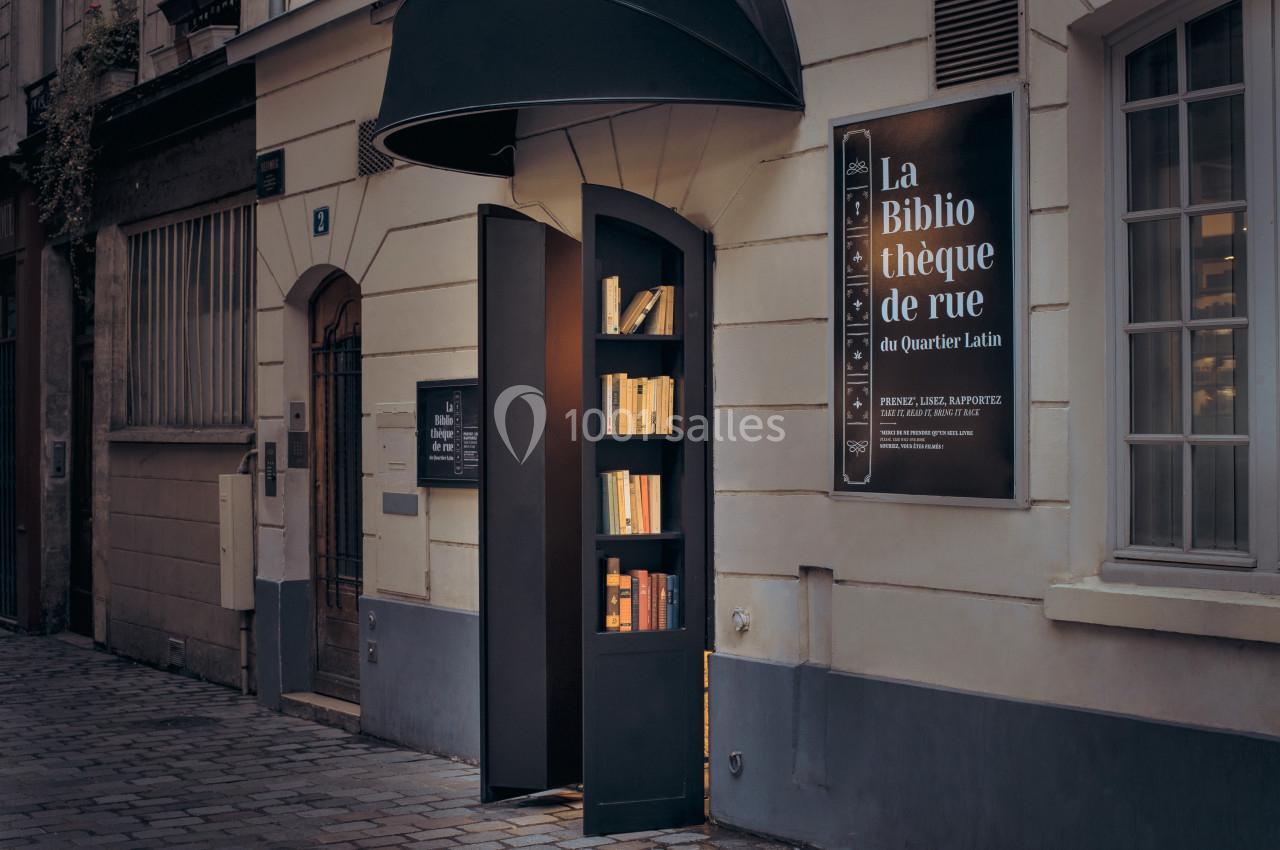 Une petite bibliothèque de rue intégrée dans un mur, éclairée, avec des livres visibles sous un auvent noir.