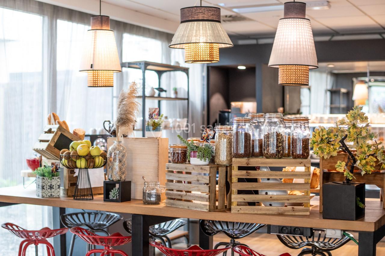 Buffet avec bocaux de céréales, fruits et décorations sur une table en bois, éclairé par des suspensions lumineuses.