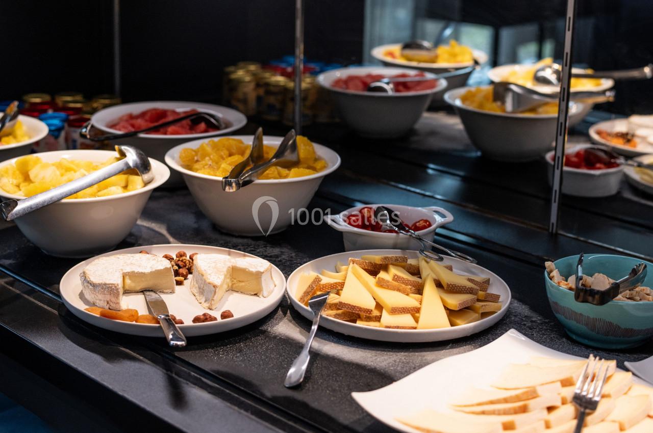 Buffet avec fromages, fruits frais, noix et condiments disposés dans des assiettes et bols sur un comptoir.