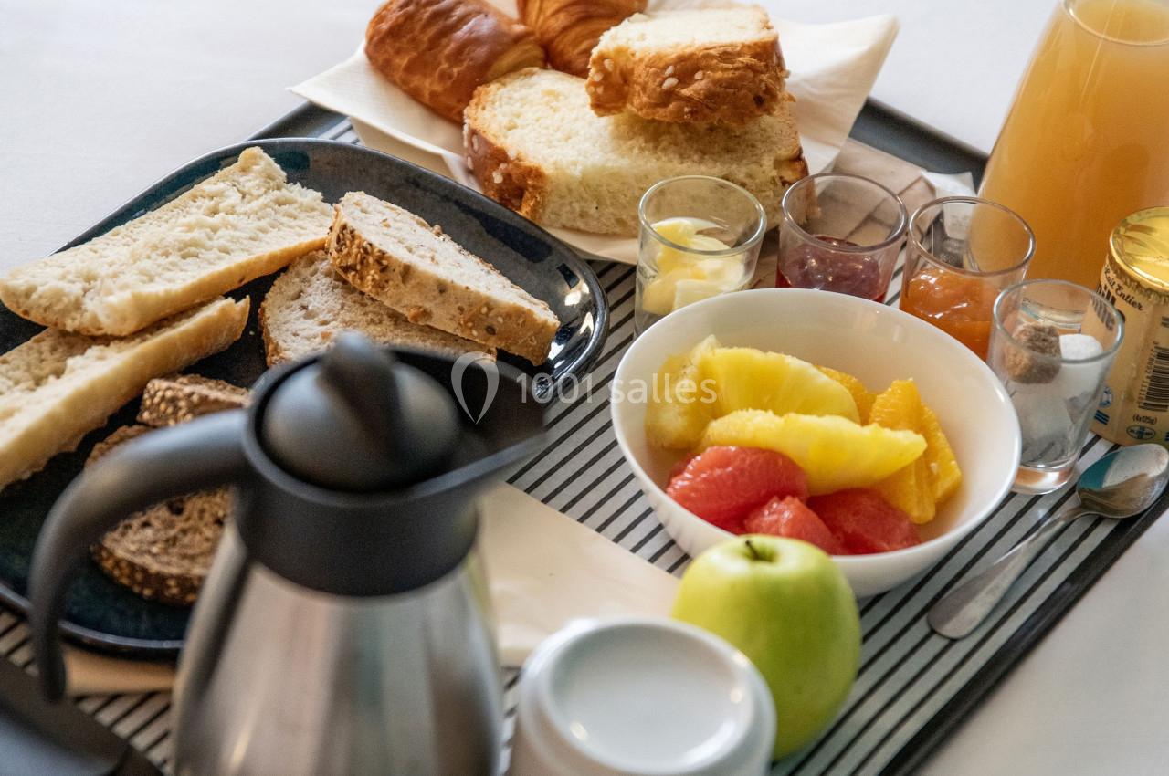 Petit-déjeuner servi sur un plateau avec pain, viennoiseries, fruits, jus d'orange, théière et condiments.