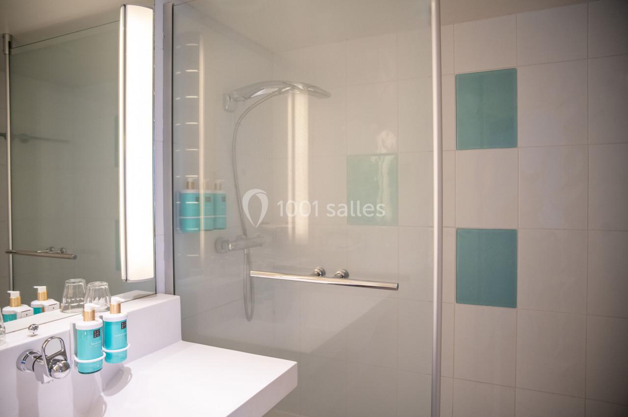 Douche moderne avec paroi vitrée, carrelage blanc et bleu, et lavabo équipé de produits de toilette.