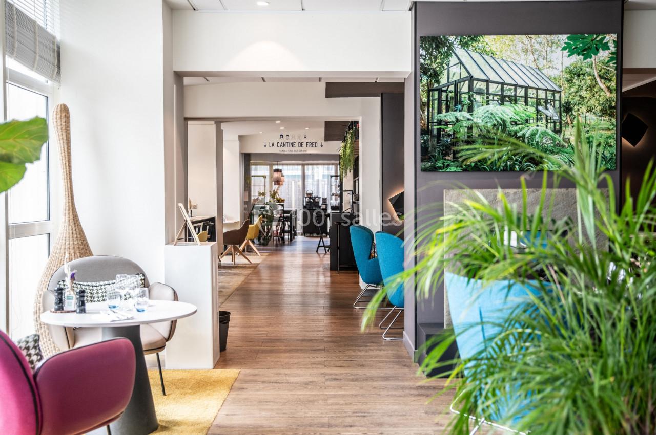 Espace intérieur lumineux avec mobilier moderne, plantes vertes et vue sur une salle à manger au fond.