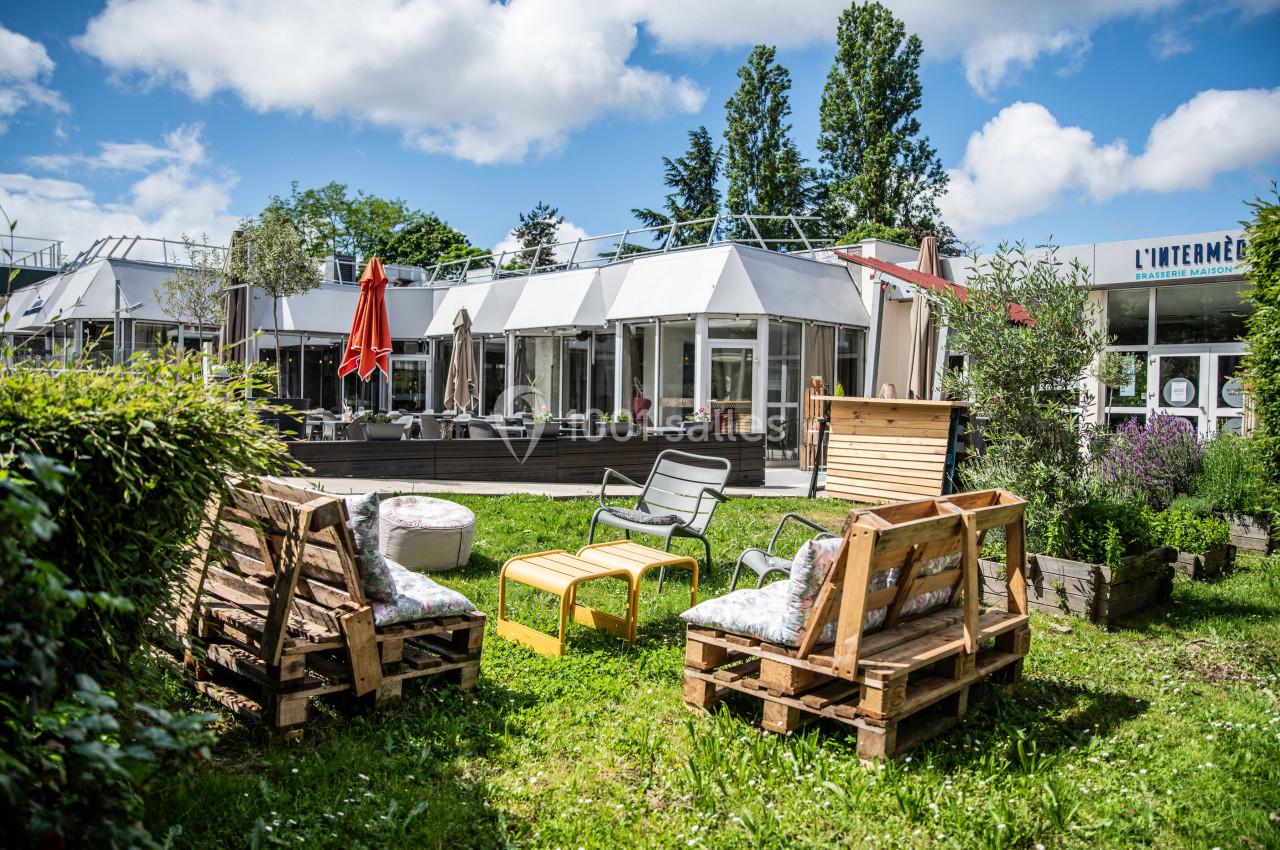 Espace extérieur avec mobilier de jardin en palettes, tables et chaises, entouré de verdure et d'arbres.