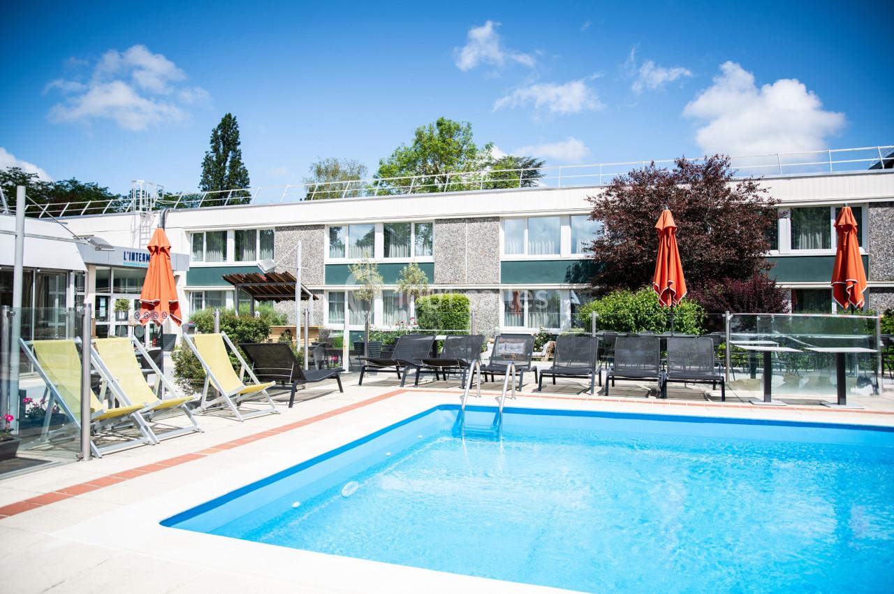 Piscine extérieure entourée de chaises longues et parasols, avec un bâtiment moderne en arrière-plan.