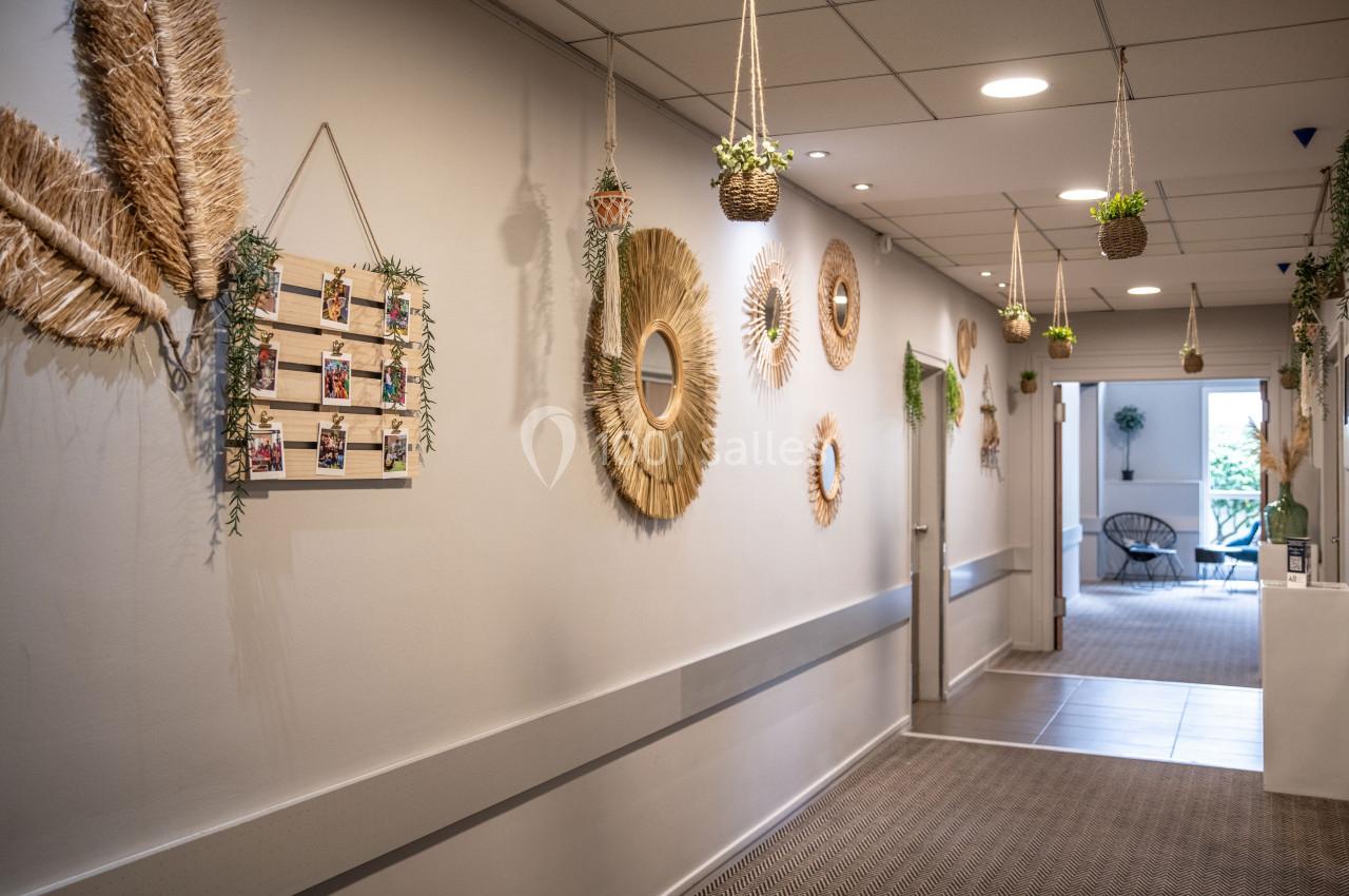 Couloir décoré avec des miroirs en rotin, des plantes suspendues et des cadres en bois sur un mur blanc.