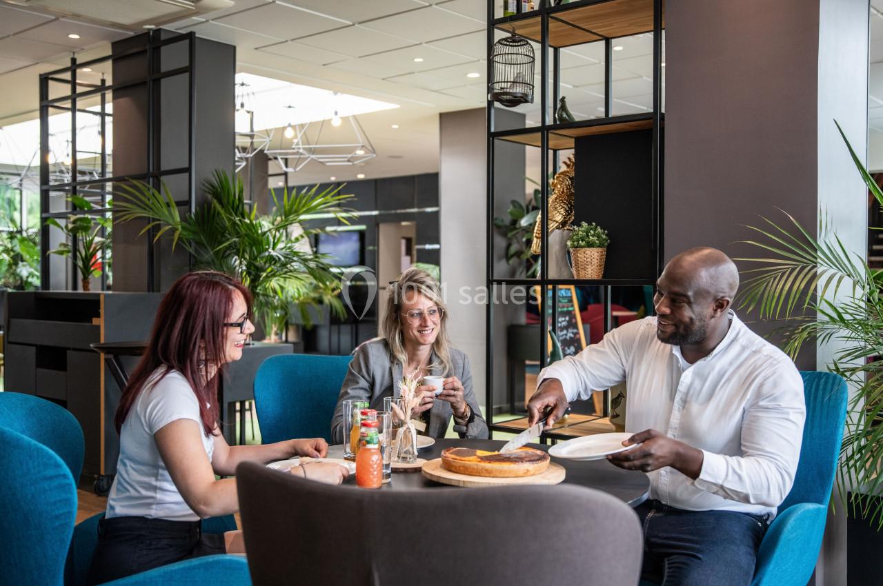 Trois personnes partagent un moment convivial autour d'une table dans un espace moderne et lumineux avec des plantes.
