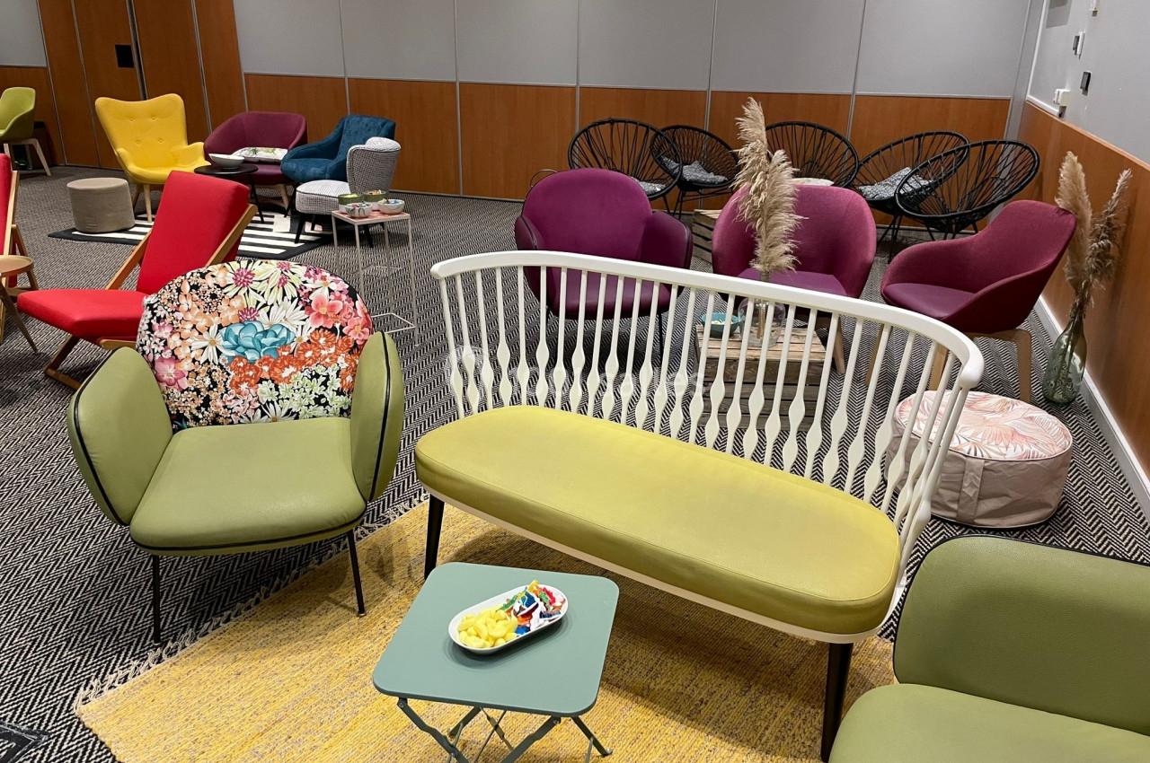 Salle aménagée avec des fauteuils colorés, un canapé, des tables basses et une décoration moderne et chaleureuse.