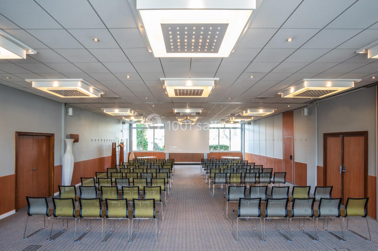 Salle de conférence lumineuse avec rangées de chaises alignées, murs clairs et plafonniers modernes.