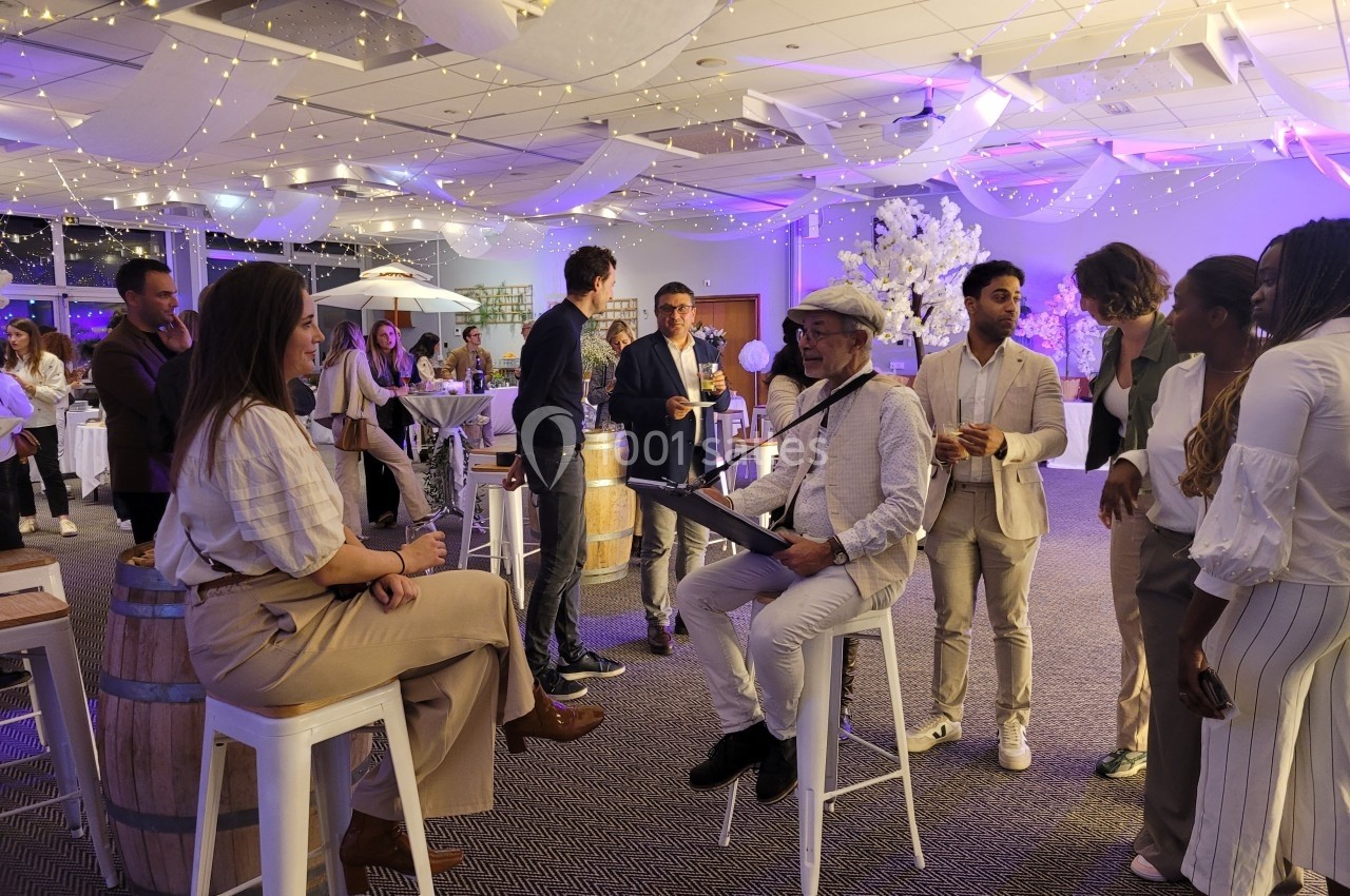 Un artiste dessine une femme assise dans une salle décorée, entourée de personnes discutant debout.
