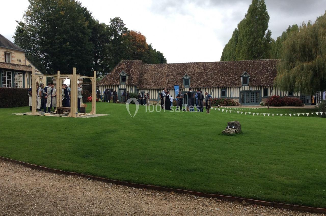 Personnes rassemblées dans un jardin devant une maison à colombages, sous un ciel nuageux.